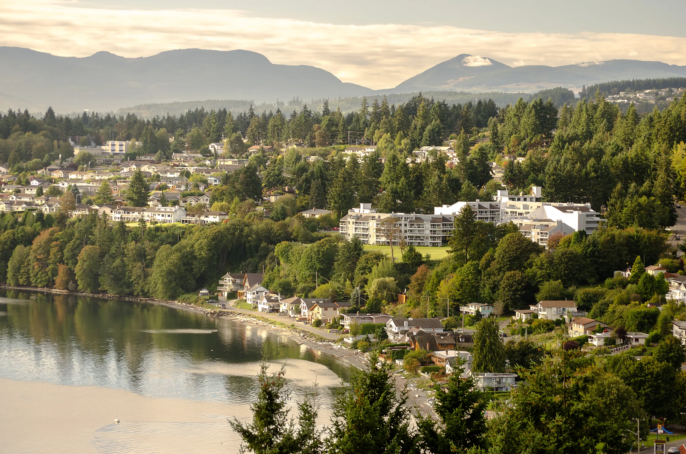 Aerial view over a Nanaimo waterfront neighbourhood with forested hills and mountains beyond